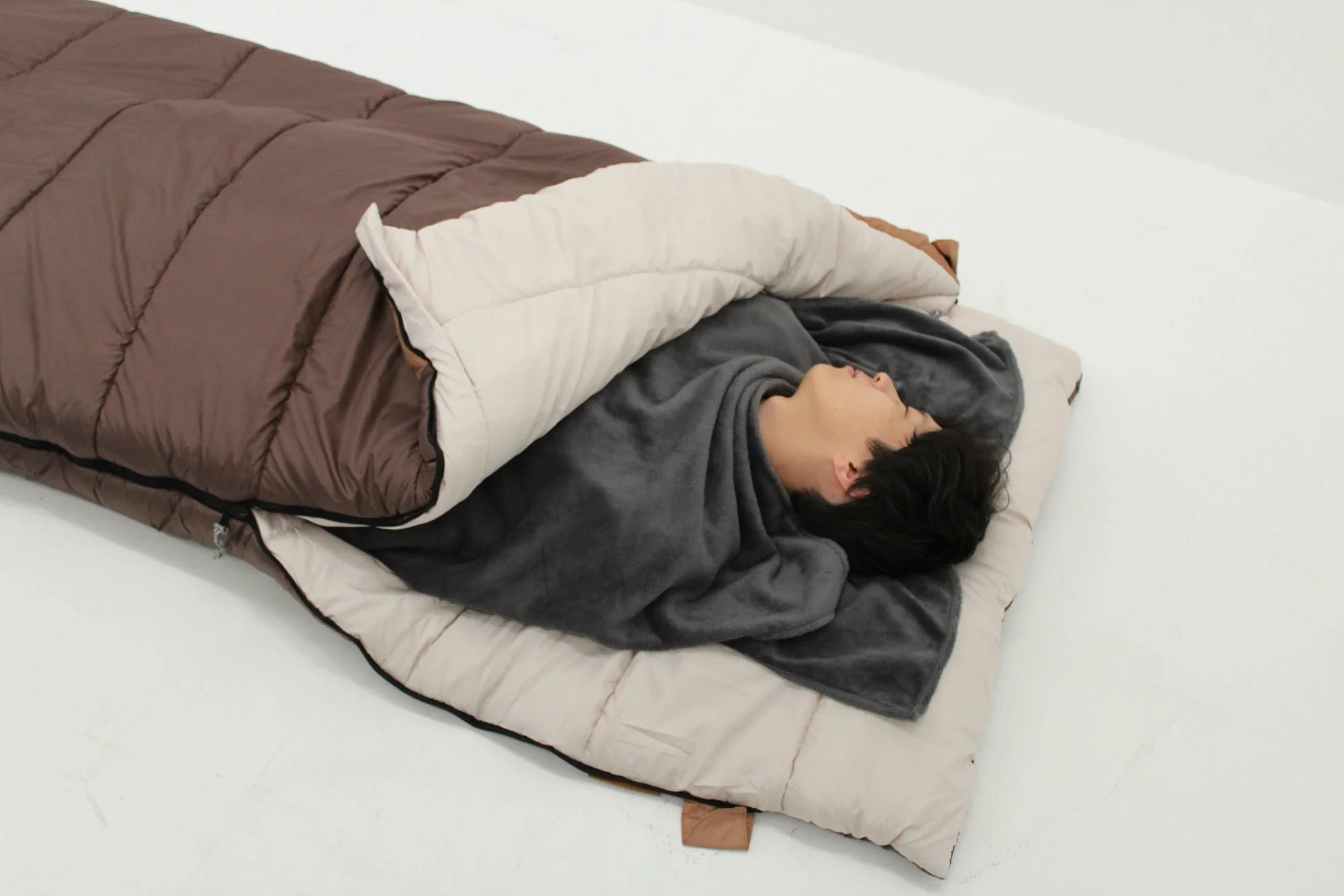 寝袋に毛布をかけて眠る男性