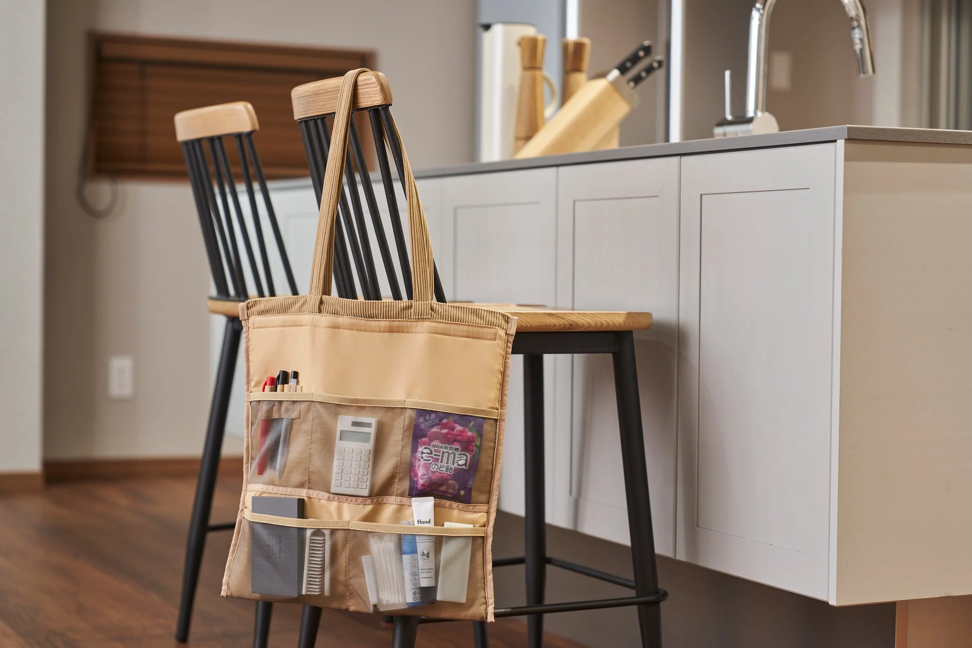 キッチンカウンターの前に置かれたスツールに、電卓やのど飴、文房具などの小物が整理されたベージュの多機能トートバッグが掛かっています。