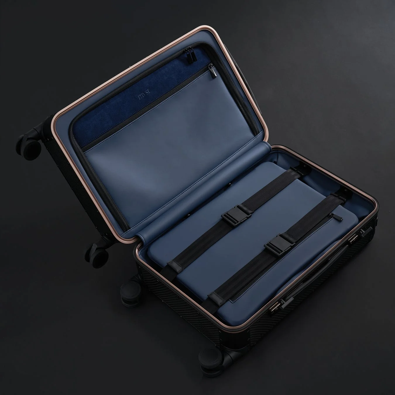 開かれた状態のスタイリッシュなスーツケースで、黒い外装にネイビーの内部、そしてローズゴールドの縁取りが特徴です