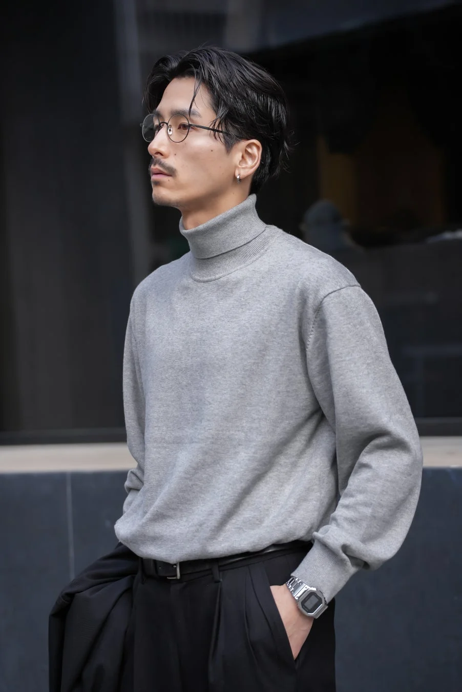 グレーのタートルネックセーターと黒いパンツを着用した男性