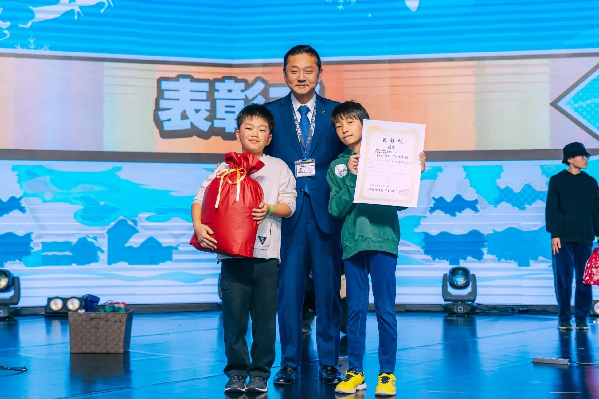 表彰式で笑顔の男性と少年たち