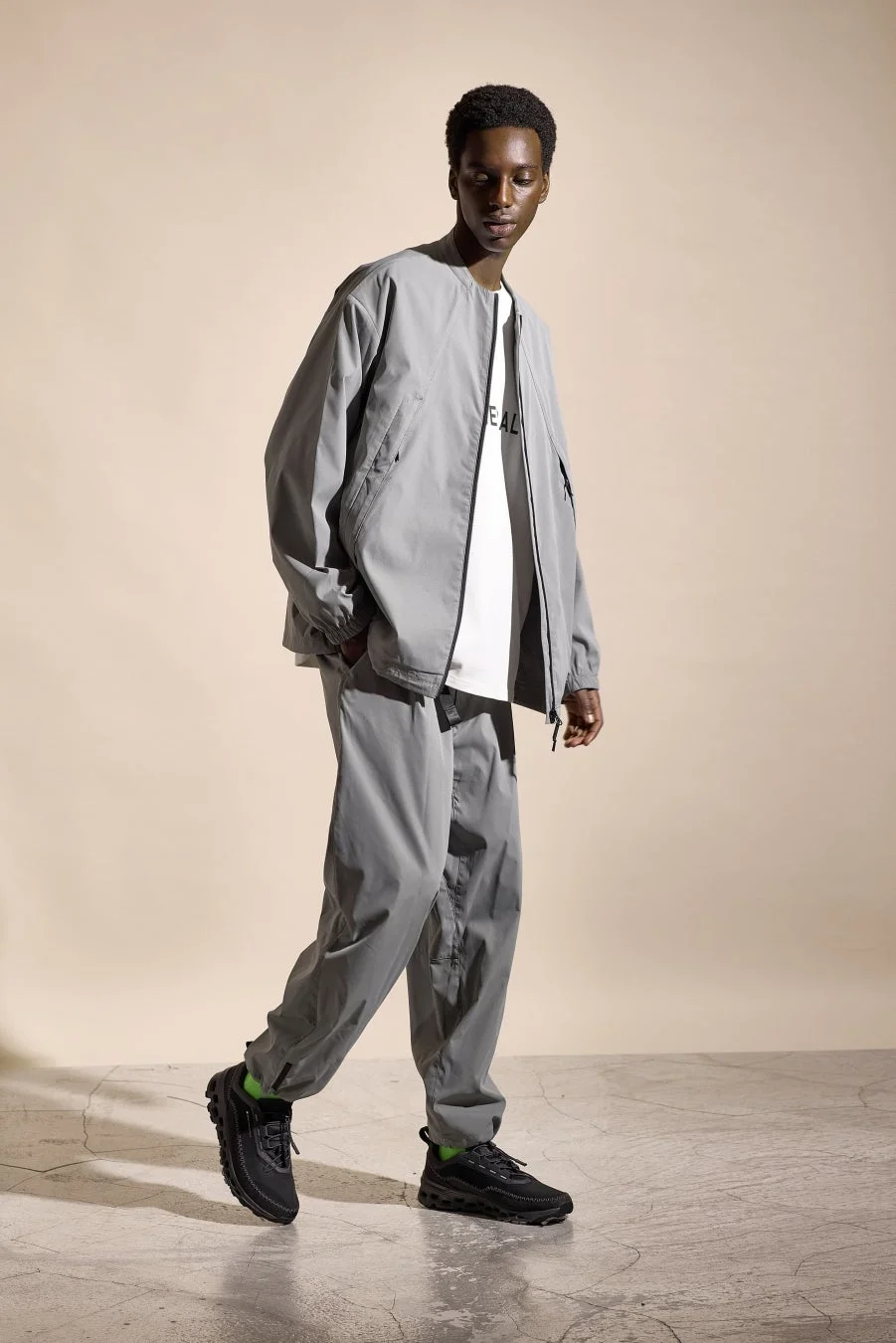 グレーのノーカラーブルゾンとワイドパンツの男性