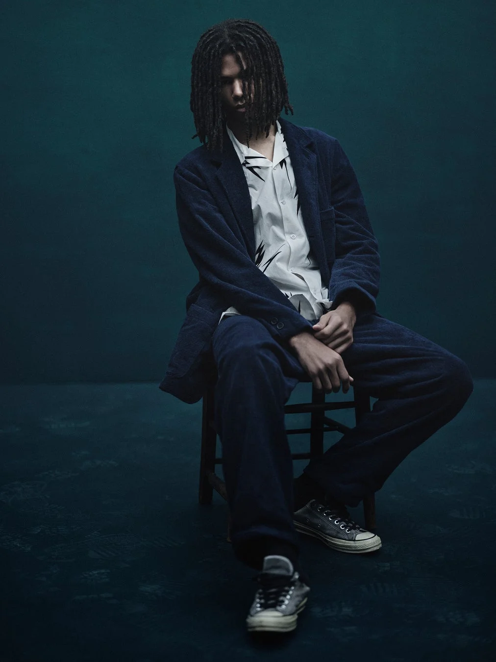 コーデュロイ風のセットアップを着用し、椅子に座る男性モデル