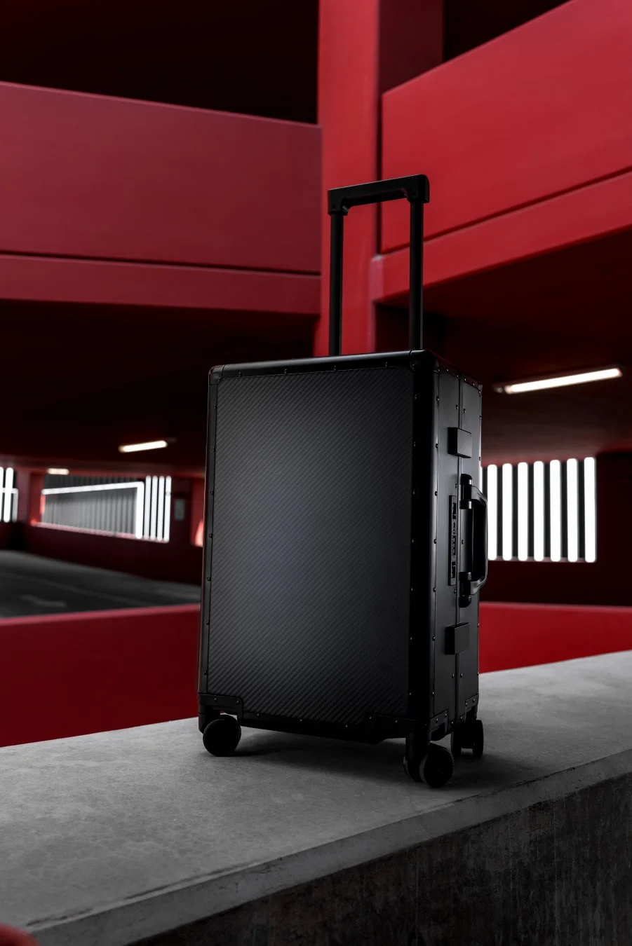 赤い壁とコンクリートのモダンな空間に、黒いカーボン調のスーツケースが置かれています