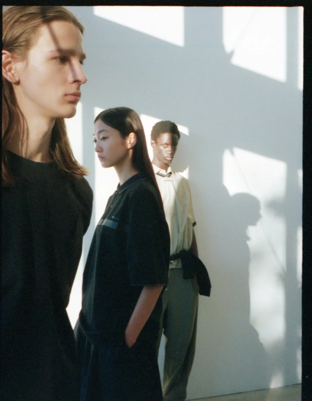 白壁を背景に並んで立つ3人のモデル