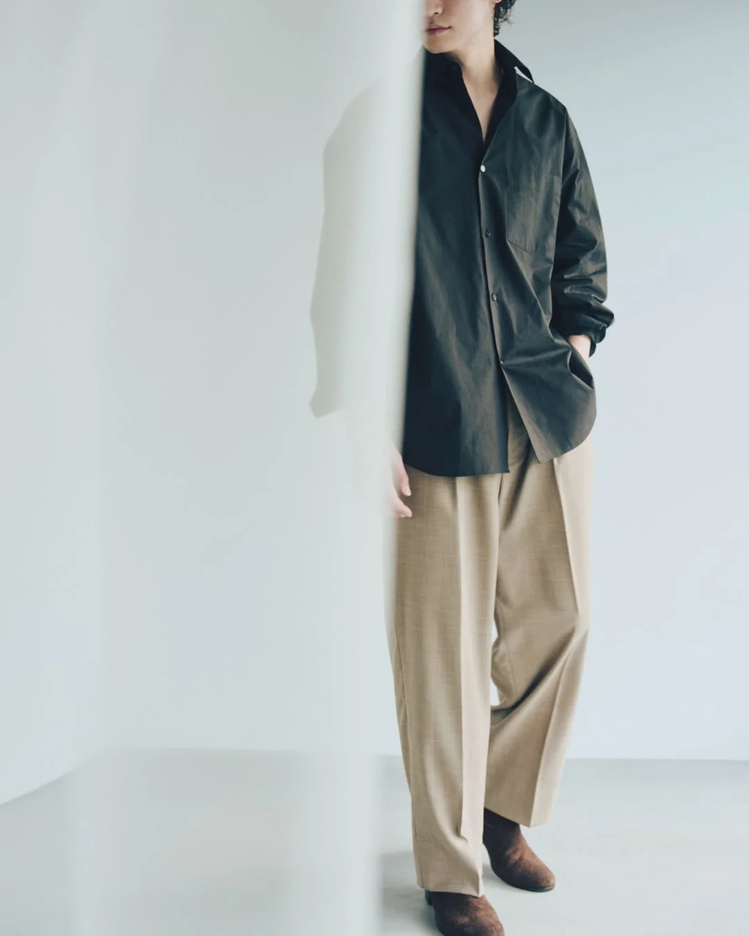 ダークブラウンのシャツとベージュのワイドパンツを着用した男性。