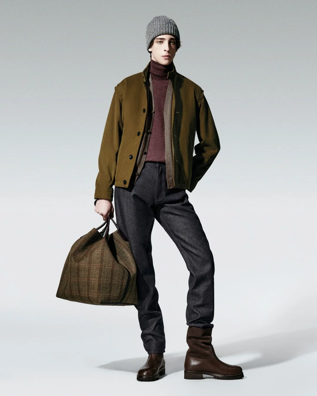 グレーのニット帽を被り、オリーブ色のジャケットとバーガンディのタートルネックを着用した男性