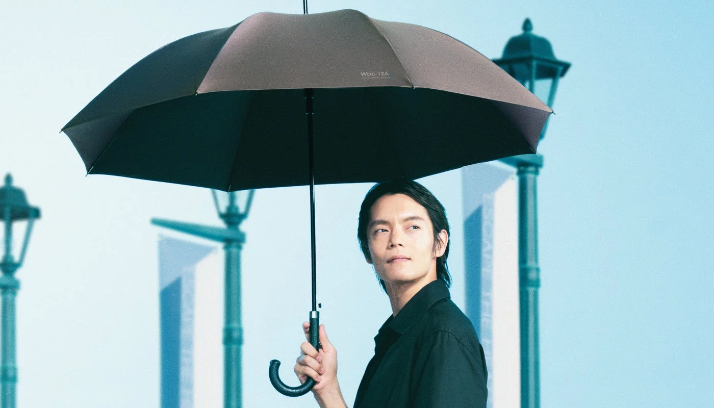 黒いシャツを着た男性がWpc.IZAの茶色い傘を差している