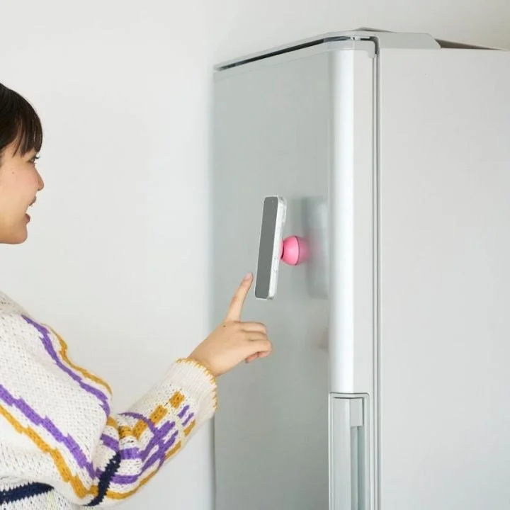 女性が冷蔵庫の側面にマグネットで取り付けられたスマートフォンを指で操作している