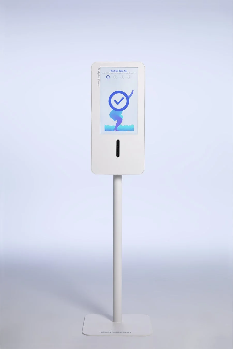 白いスタンド型のデジタルキオスクが写っており、画面には「オーバーヘッドスクワットテスト」の指示とイラストが表示されています