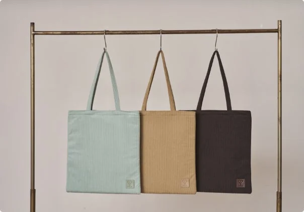 3色の異なるシンプルなトートバッグが金属製のラックに吊り下げられています。