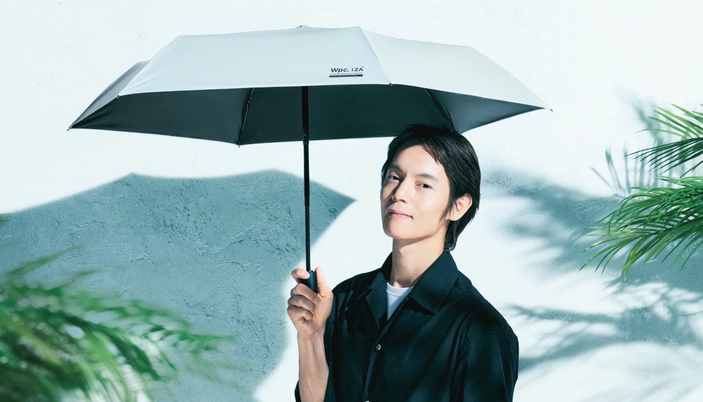 黒いシャツを着た男性がライトグレーの傘を差して微笑んでいる広告写真