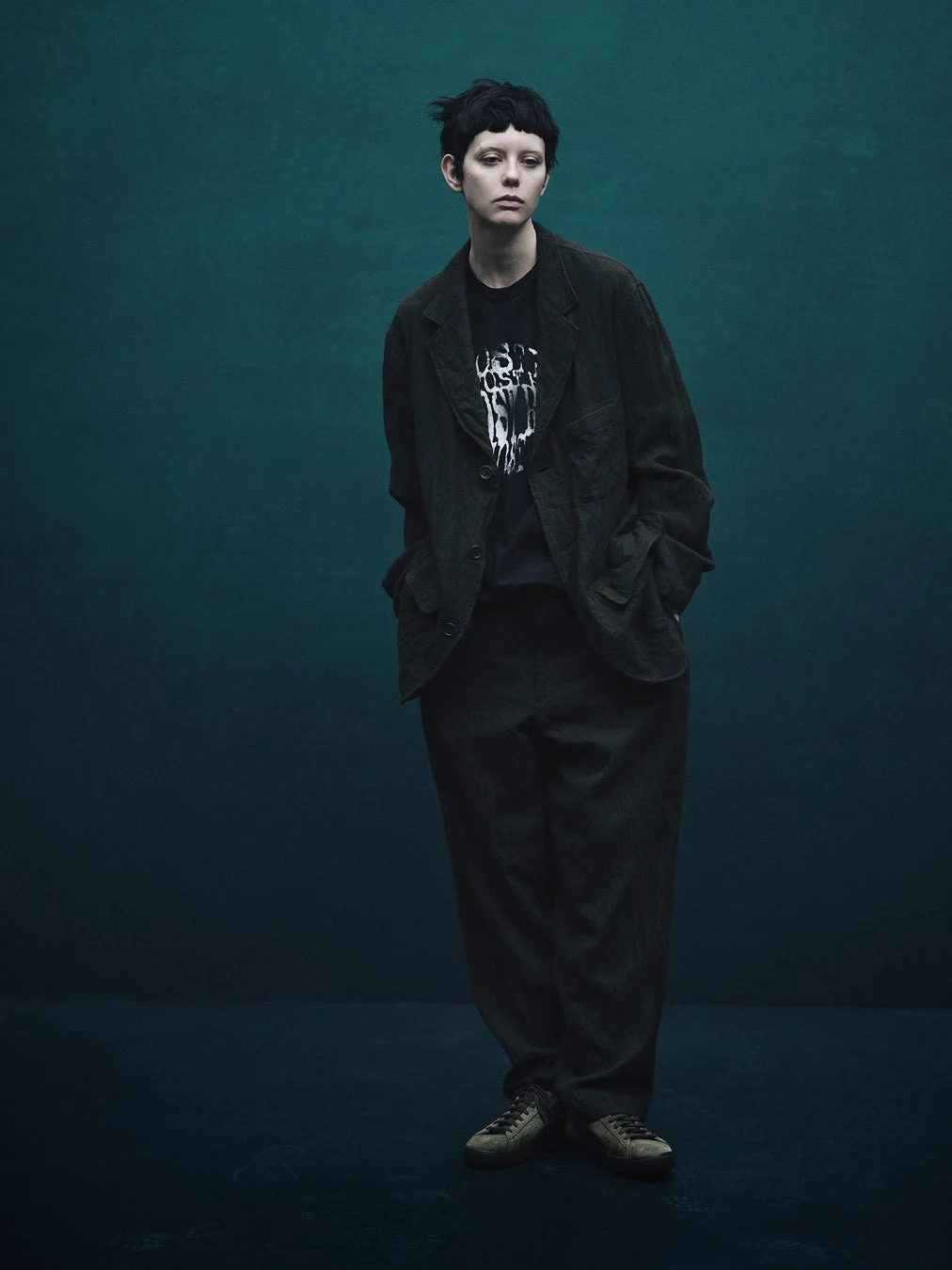 深緑の背景でブレザーとワイドパンツを着用したモデル