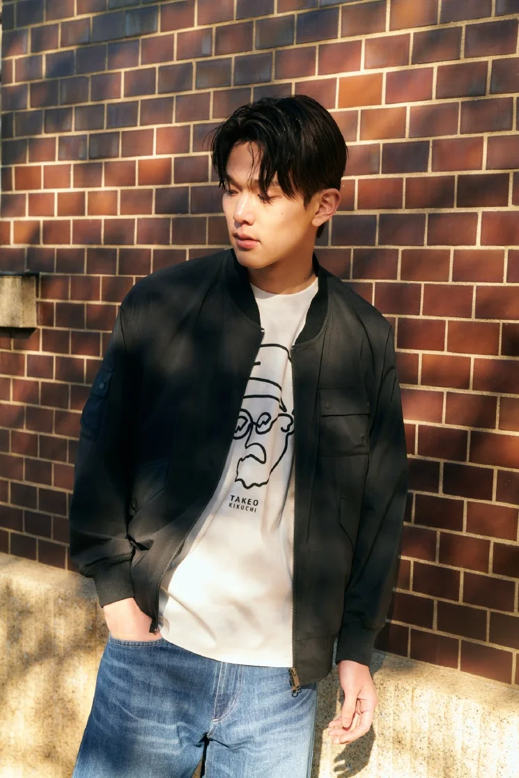 レンガの壁を背景に黒いブルゾンを着た男性