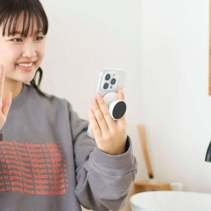 笑顔の若い女性が、スマホグリップを取り付けたスマートフォンを手に持っている
