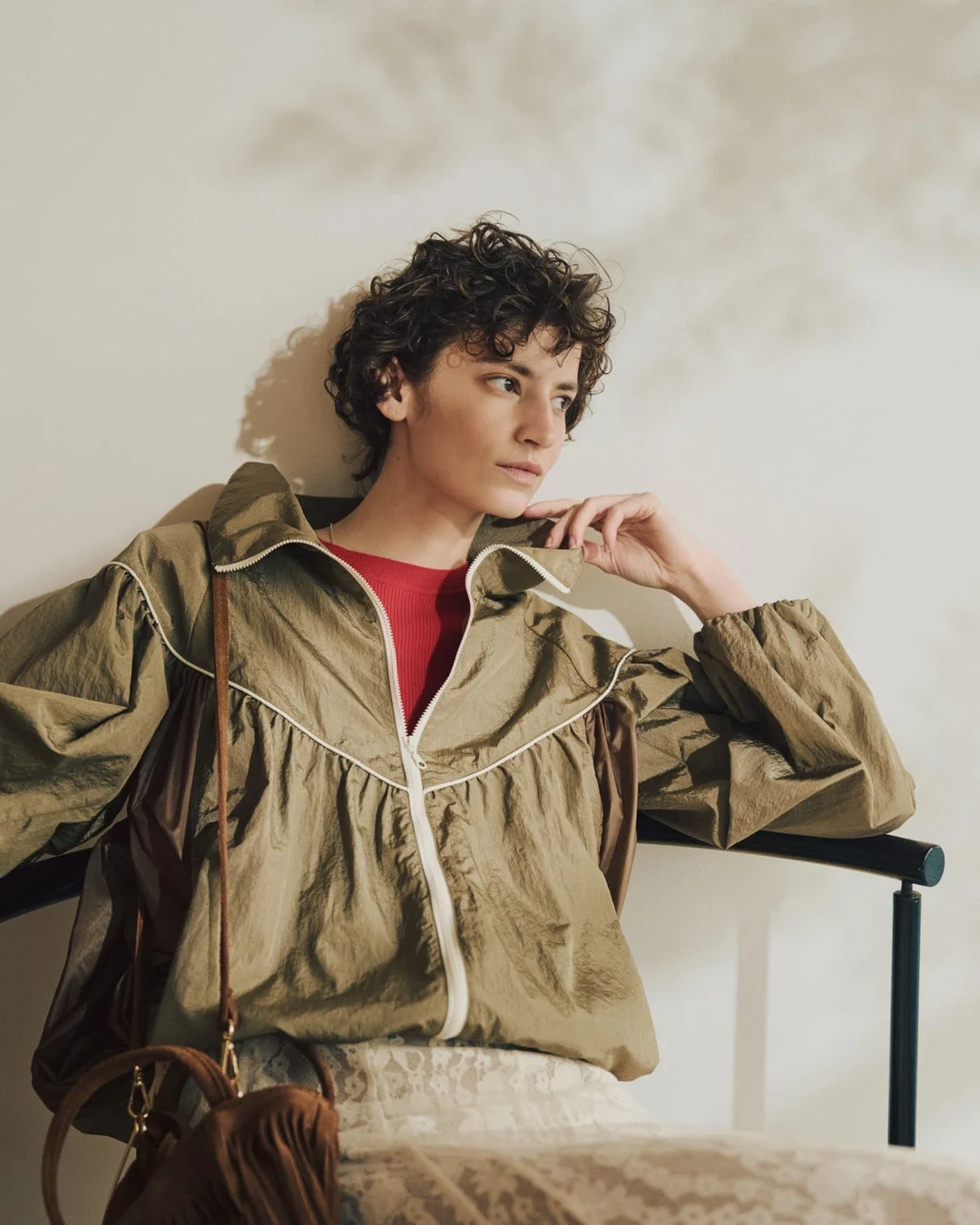 カーキ色のジップアップジャケットと赤いトップスを着用したショートヘアの女性。