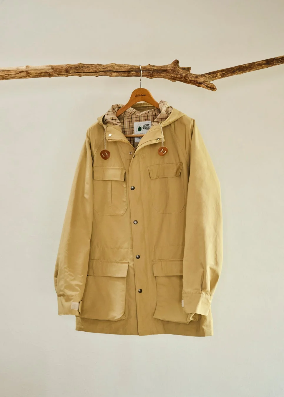 ベージュ色のフード付きマウンテンパーカーが木の枝に掛けられています。