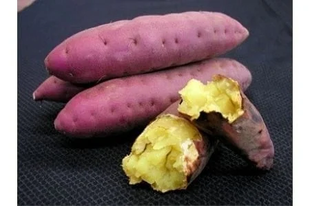 黒い背景の上に、皮が紫色のさつまいもが数本置かれており、そのうちの2本は割れて中から黄色く焼けた部分が見えています