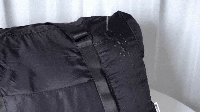 黒い生地のバッグに水がかけられ、水滴が弾かれている様子