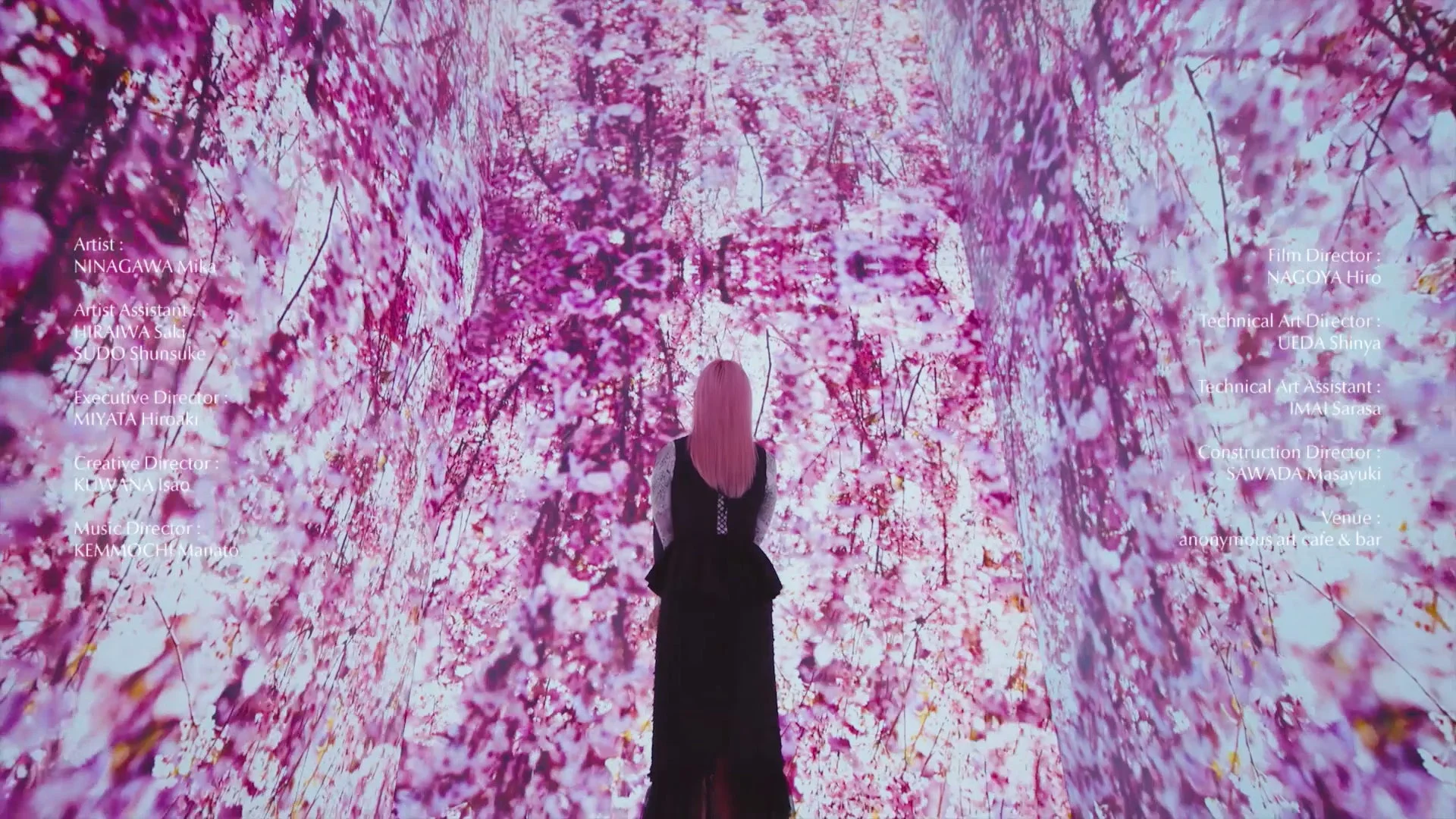 桜のプロジェクションマッピングに囲まれた幻想的な空間に立つピンク髪の女性と作品クレジット