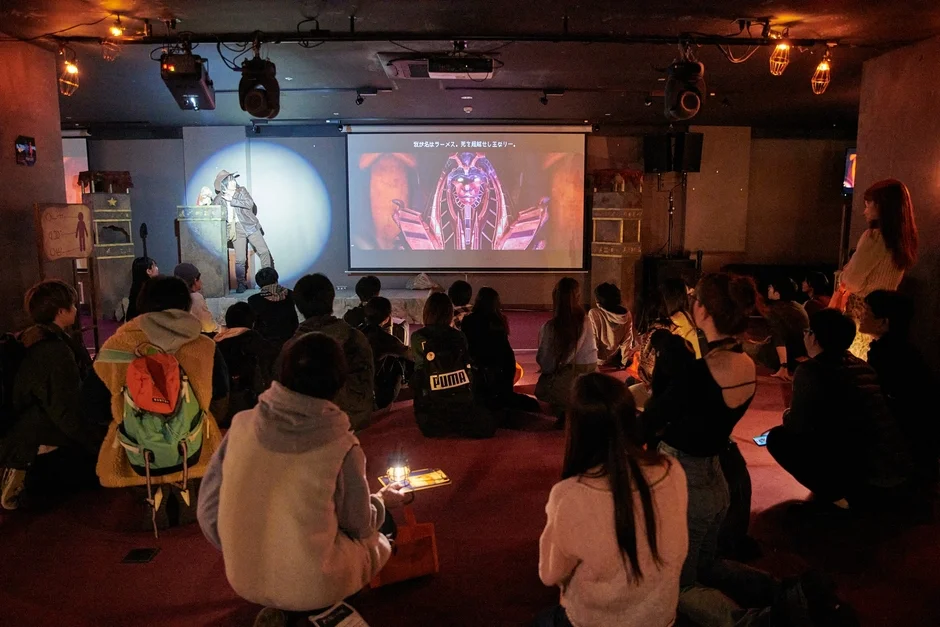 イベント会場でスクリーンを見る観客とパフォーマー