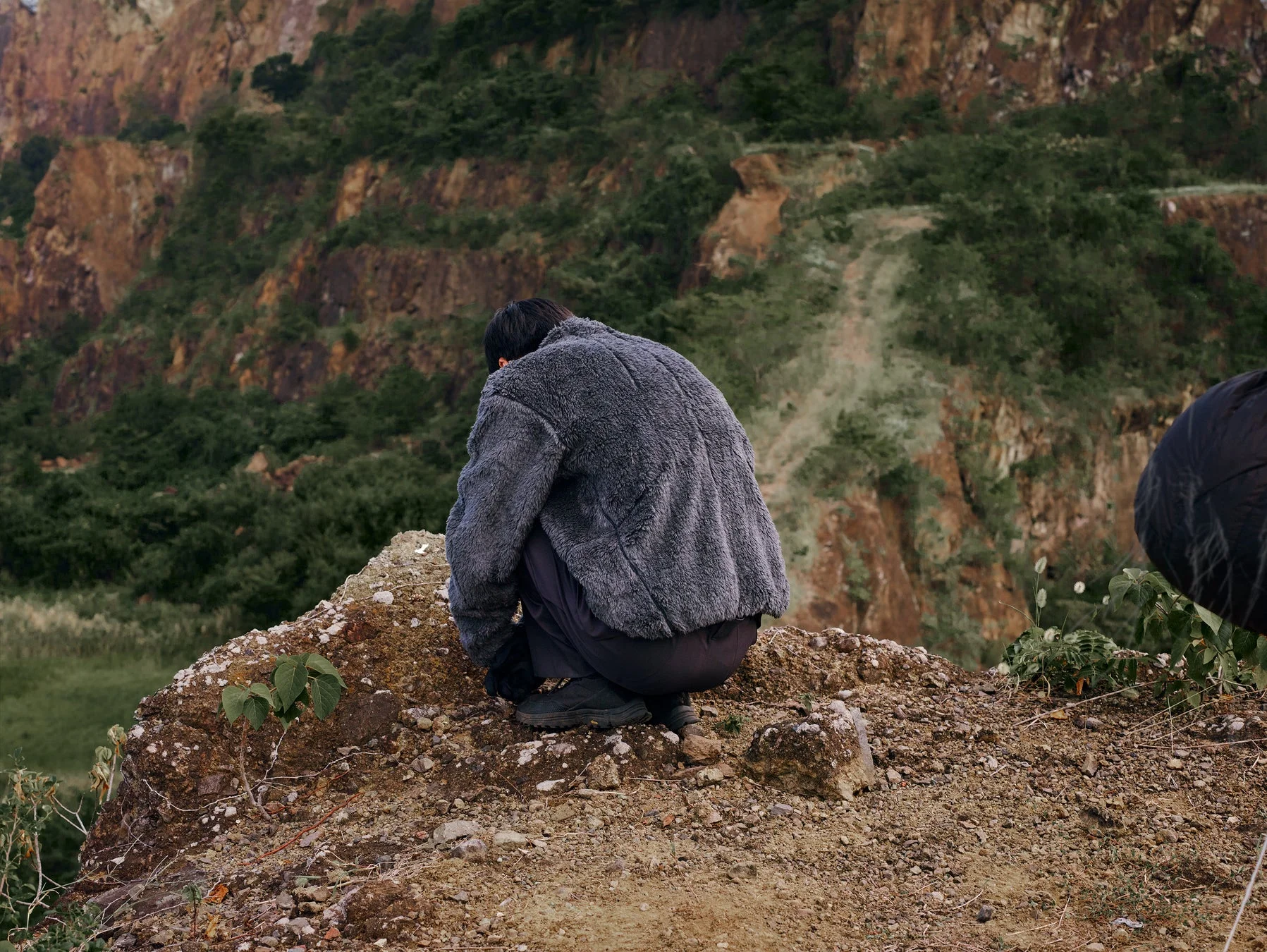 人物が岩場でしゃがむ後姿