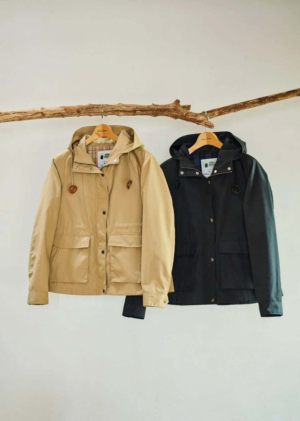 ベージュとダークグリーンのフード付きジャケットが木の枝に吊るされています。