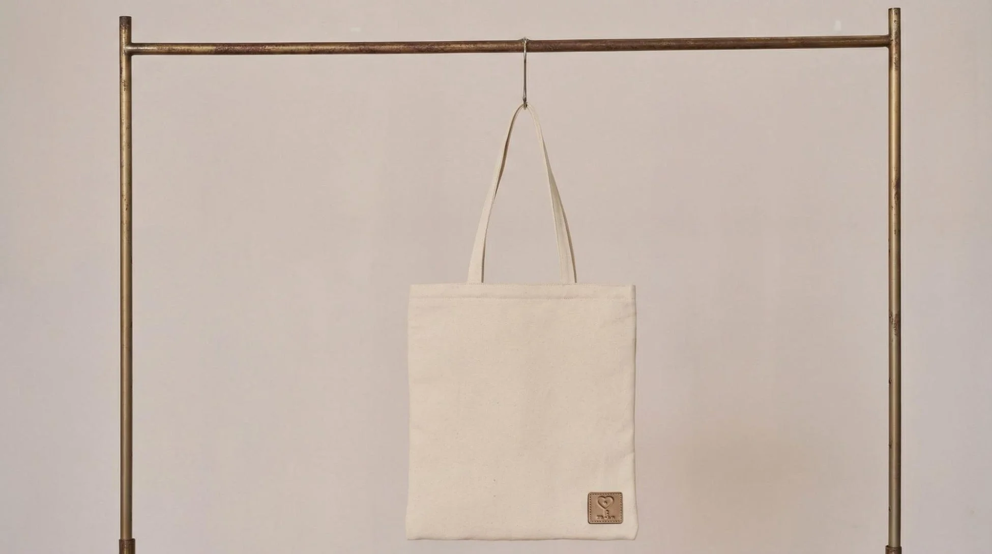 真鍮色のハンガーラックに吊るされた、無地のオフホワイトのキャンバストートバッグです。