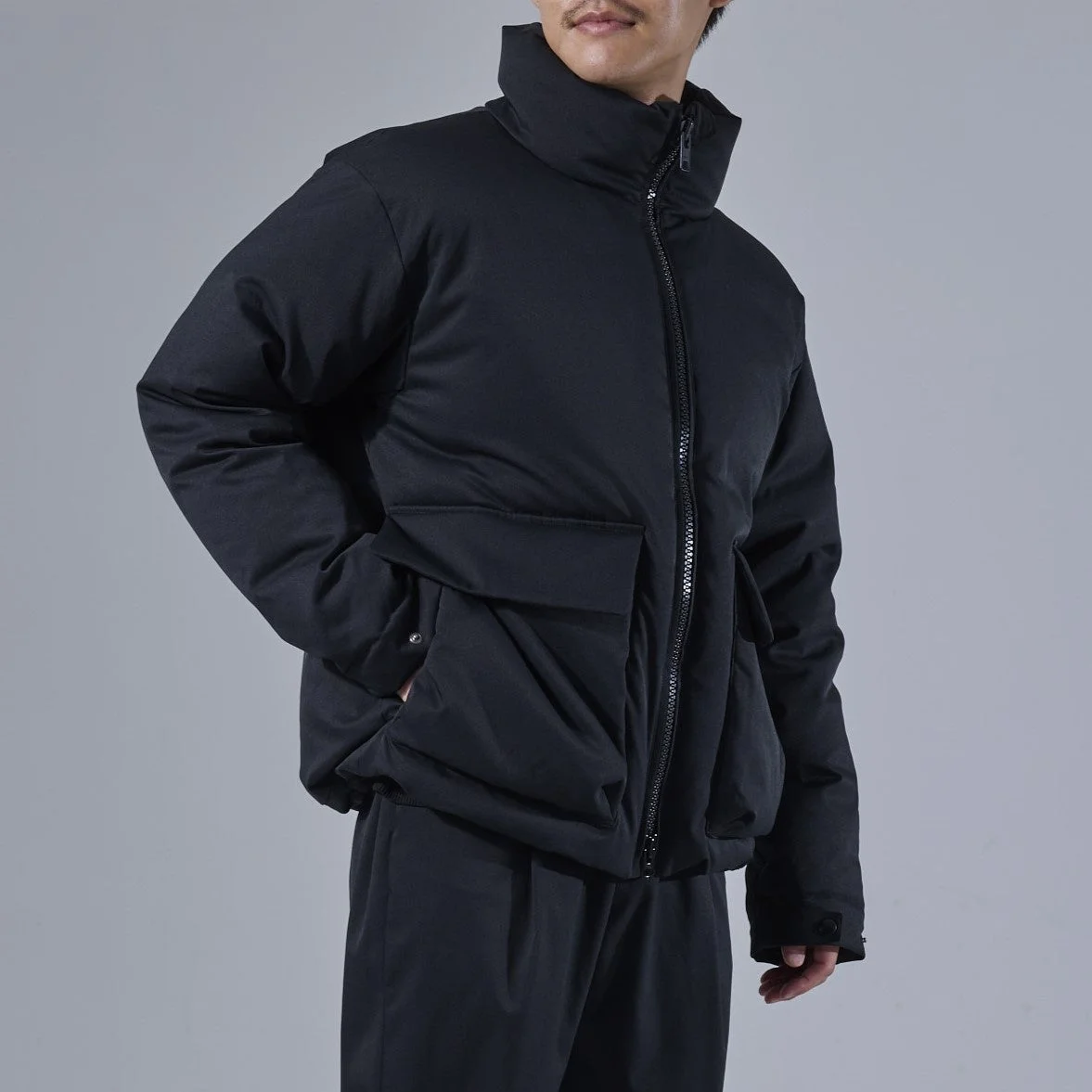 黒いスタンドカラーのダウンジャケットと黒いパンツを着用した男性