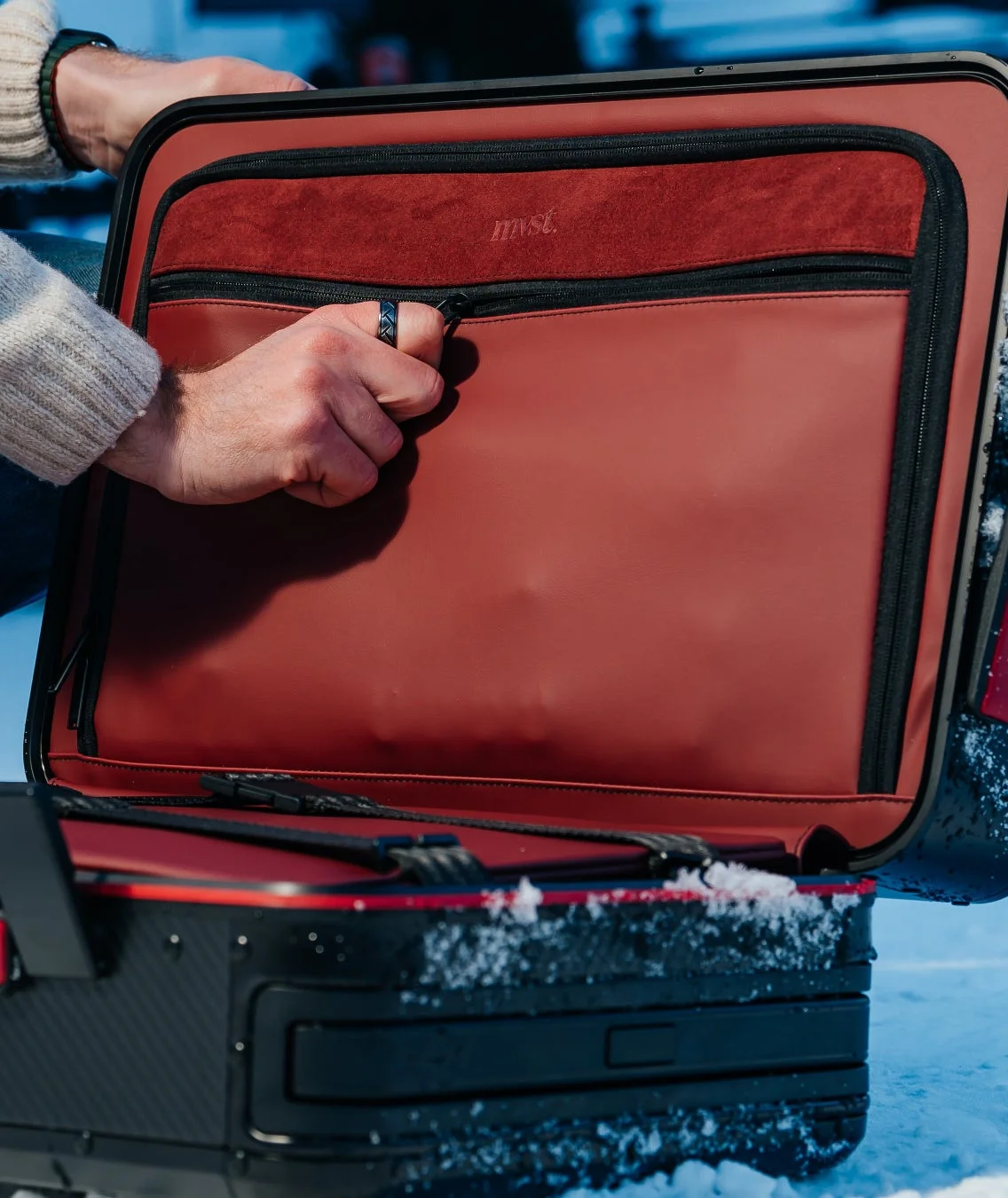 雪の上に置かれた、赤と黒のスタイリッシュなスーツケースを開ける人の手元を捉えた画像です