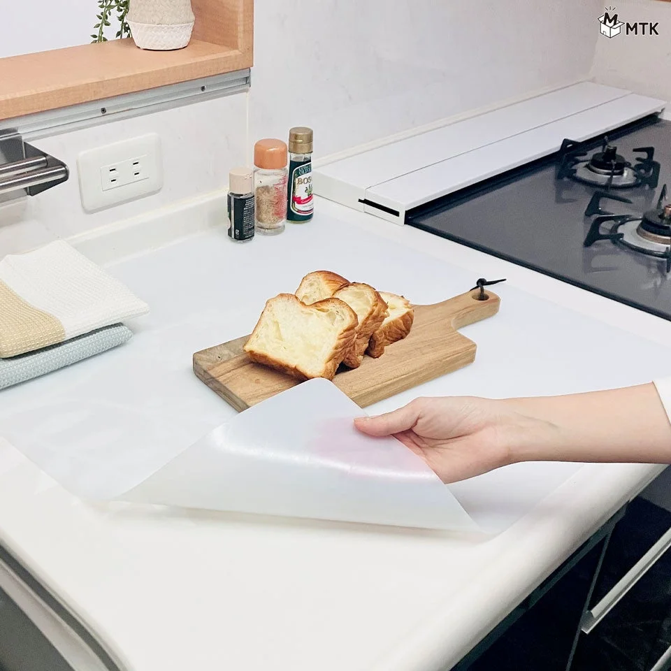 清潔感のあるキッチンの調理台で、パンとまな板の横に半透明のマットを敷く様子