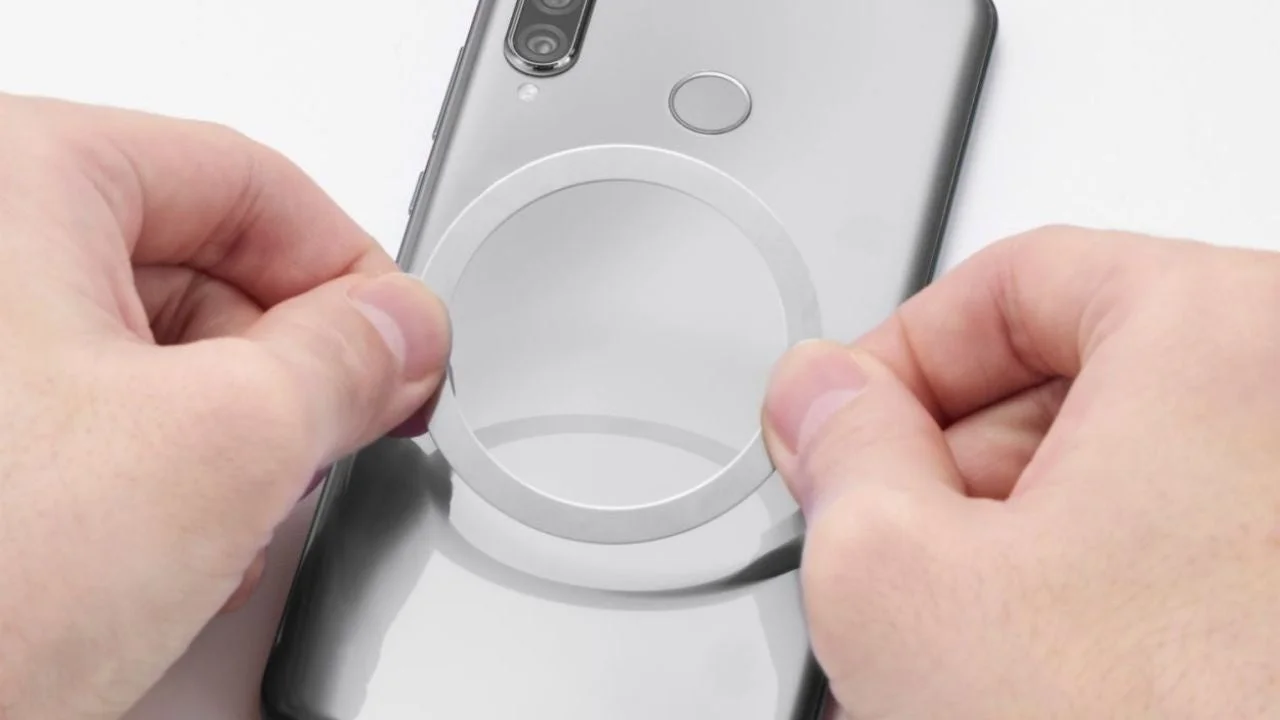 スマートフォンの背面に、円形の白いリング状のアクセサリーを貼り付けようとしている様子