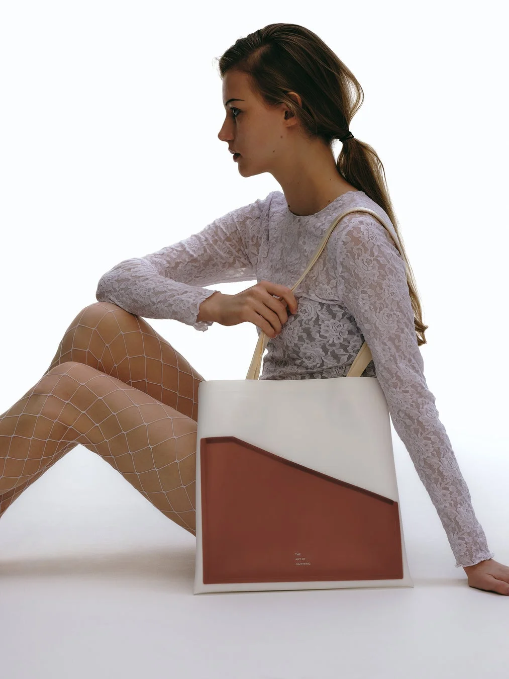 レースのトップスと網タイツを身に着けた女性が座ってトートバッグを持っている画像