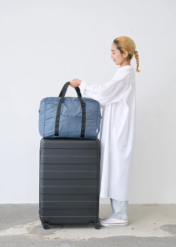 女性が黒いスーツケースの上に置かれた水色のボストンバッグを手に持っている