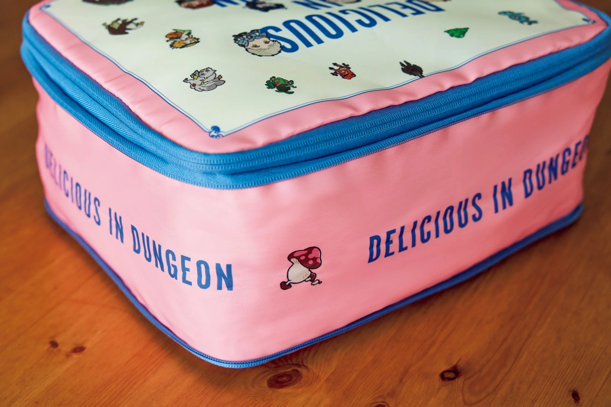 ダンジョン飯のキャラクターがデザインされたピンク色の収納ポーチ