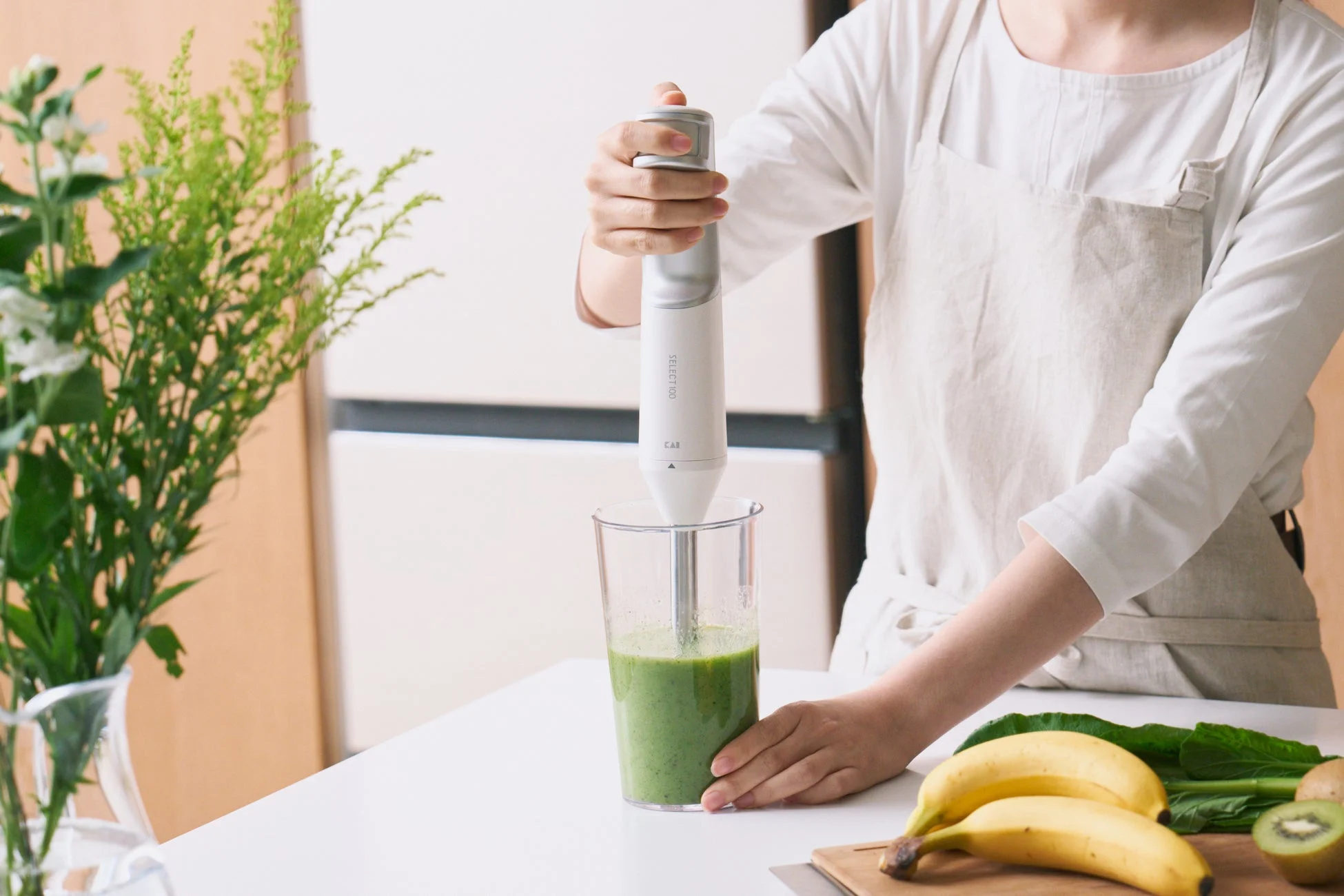 エプロンを着た人物がハンドブレンダーを使ってグリーンスムージーを作っている様子
