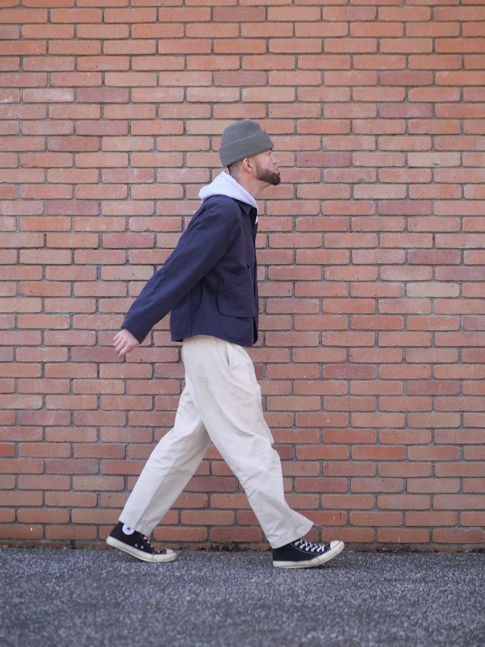 レンガの壁を背景に歩く男性の全身像